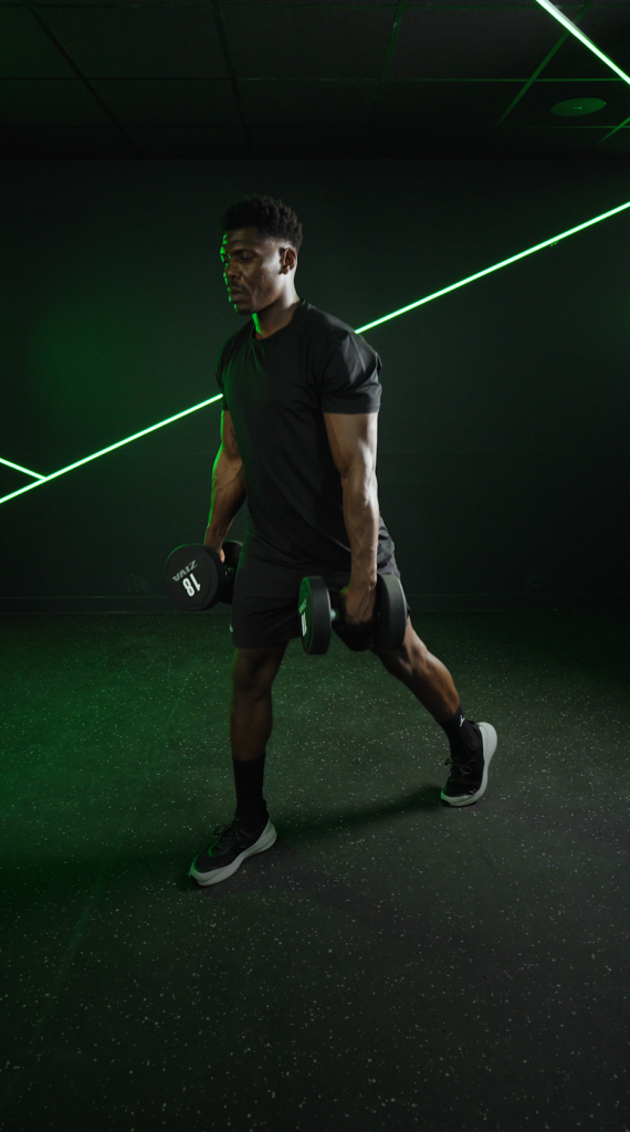 An athlete in a forward lunge, dumbbells in hand, in a dark room with green neon