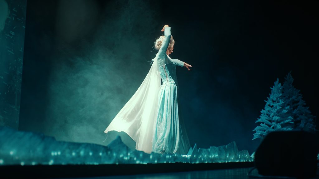 An actress in a sparkling white gown centre stage, surrounded by bluish mist