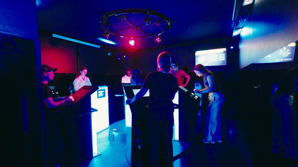 Players in front of glowing terminals in a room lit in blue and red