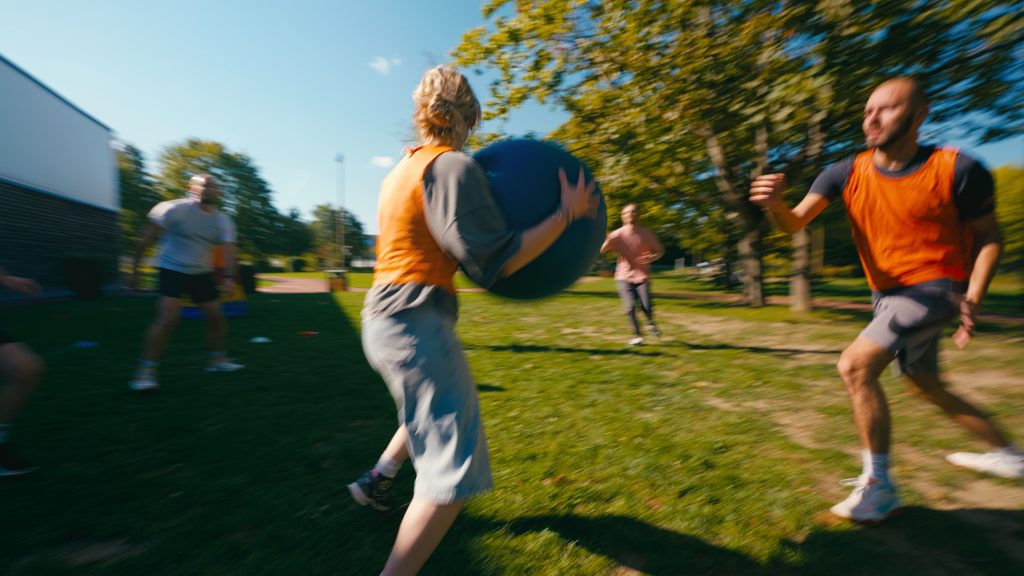 A participant running with a big blue ball in a park during a team game