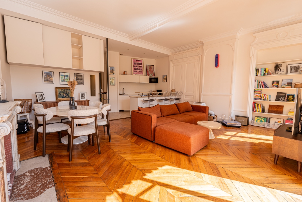 Grand séjour au parquet en chevrons, canapé orange et bibliothèque