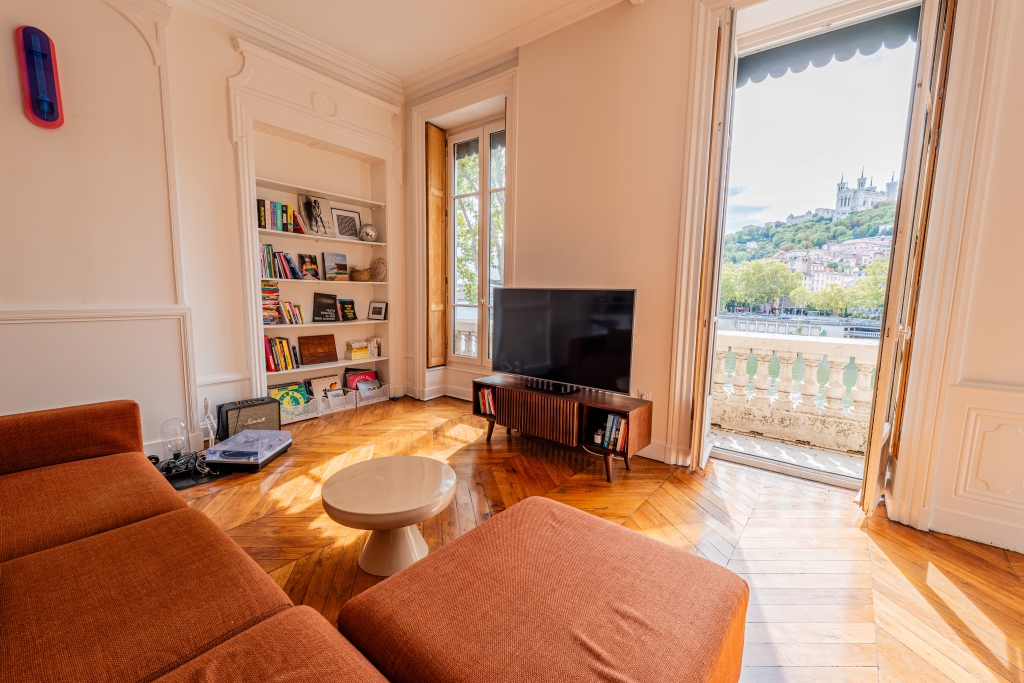 Salon lumineux avec bibliothèque et porte-fenêtre ouverte sur la colline de Fourvière