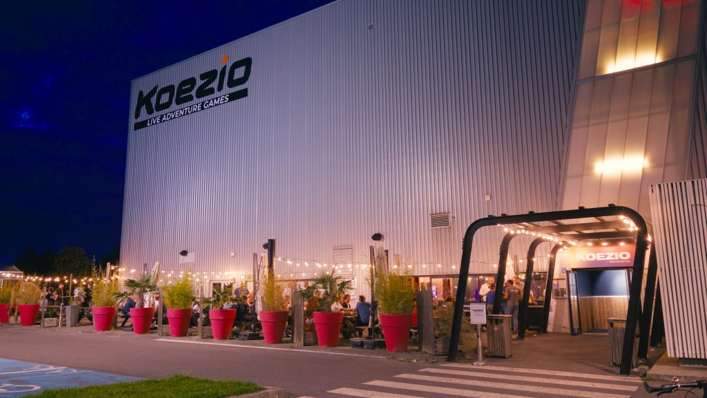 The Koezio building lit at dusk, with a terrace decorated with string lights