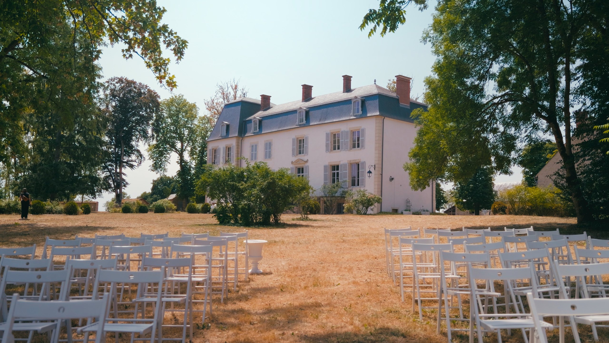 White chairs set up for the outdoor ceremony in the grounds of Domaine de Mont, in front of the château